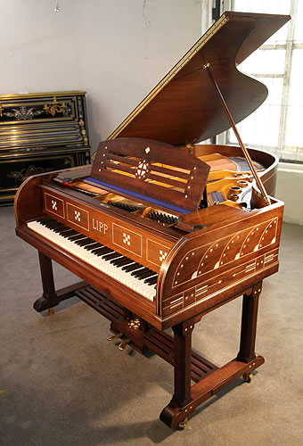 An Arts and Crafts, Lipp grand piano for sale with a mahogany case inlaid with geometric designs. Case features ornate brass hinges and slatted cross stretcher. Piano has an eighty-five note keyboard and a two-pedal piano lyre.