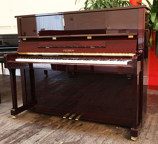 Brand New Feurich Model 122 upright piano with a Bordeaux Gloss mahogany case and brass fittings. Piano has an eighty-eight note keyboard and three pedals.