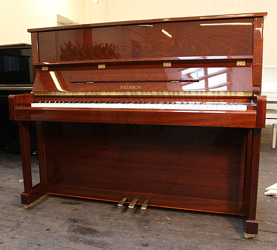 Brand new, Feurich Model 122 upright piano with a Walnut Gloss case and brass fittings. Piano has an eighty-eight note keyboard and three pedals.