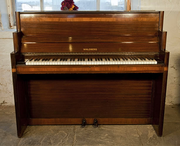 An Art-Deco Waldberg upright piano with a polished, mahogany case. Piano has an eighty-five note keyboard and two pedals