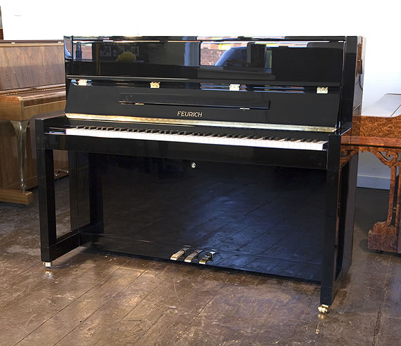 Brand New Feurich Model 115 upright piano with a black case and brass fittings. Piano has an eighty-eight note keyboard and  three pedals