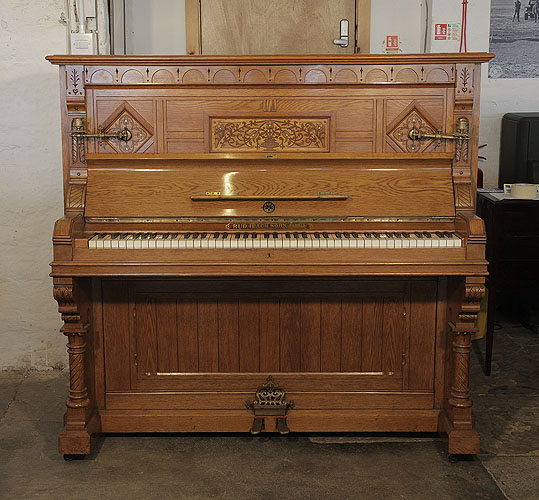 An 1895, English Gothic style, Ibach upright piano with a carved, oak case and ornate brass candlesticks and handles. Cabinet features traditional folk art motif carvings  and inlay.  Piano has an eighty-five note keyboard and two pedals.  