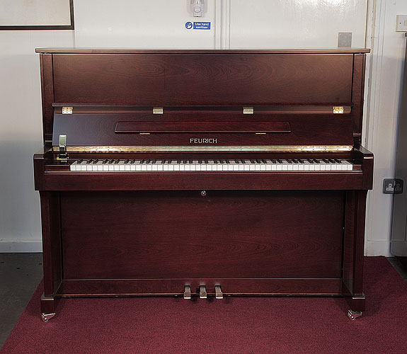 Brand new, Feurich Model 122 upright piano with a satin, walnut case and brass fittings. Piano has an eighty-eight note keyboard and three pedals. 
