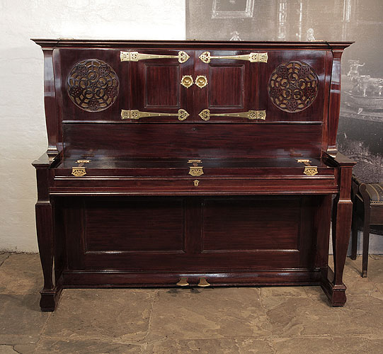 An 1897, Arts and Crafts style, Bechstein upright piano with a rosewood case, fretwork panels and ornate brass hinges in a stylised floral design. Unique design by Walter Cave, executed by C. Bechstein and exhibited by Maple & Co. Piano has an eighty-eight note keyboard and two pedals. 