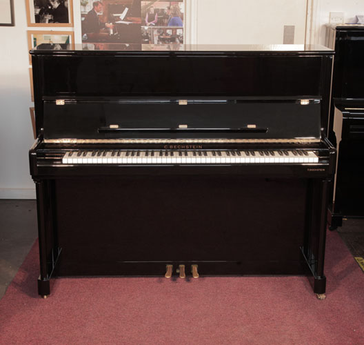 A 2001, Bechstein Elegance 124 upright piano for sale with a black case and brass fittings. Piano has an eighty-eight note keyboard and three pedals. 
