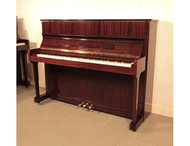 A 1989, Legnica  M110 upright piano with a  polished, mahogany case and brass fittings. Piano has an eighty-eight note keyboard and three pedals. 