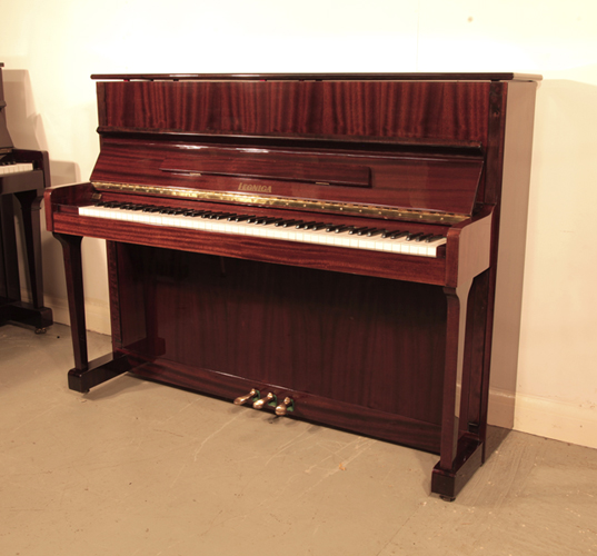 A 1989, Legnica  M110 upright piano with a  polished, mahogany case and brass fittings. Piano has an eighty-eight note keyboard and and three pedals 