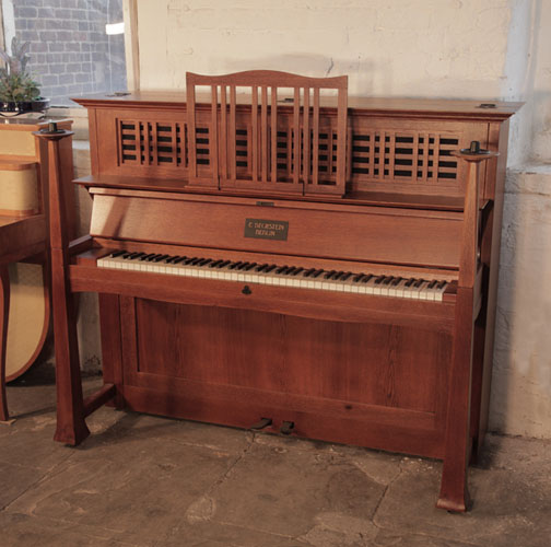 Arts and Crafts, 1905, Bechstein model 9 upright piano with an oak case and statement iron hinges. Part of the cabinet design, the large sculptural candlesticks sit atop the square piano legs. Design by Walter Cave. Piano has an eighty-five note keyboard and two pedals.