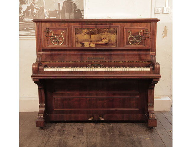 A 1905, Brinsmead upright piano with a polished, rosewood case and front panel featuring a crystoleum in Pre Raphaelite style