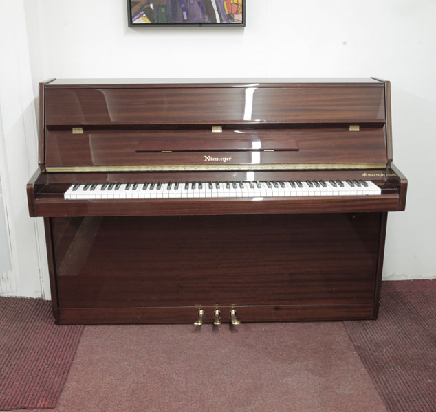 Pre-owned, Niemeyer  upright piano with a mahogany gloss case. Piano has an eighty-eight note keyboard and three pedals. 