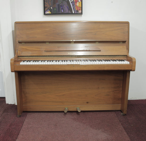 A 1981, Welmar upright piano with a polished, walnut case. Piano has an eighty-eight note keyboard and two pedals.