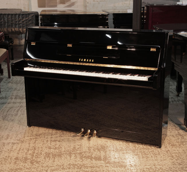 A Yamaha bl PE  upright piano with a gloss black case and brass fittings. Piano has an eighty-eight note keyboard and three pedals. Condition as new.